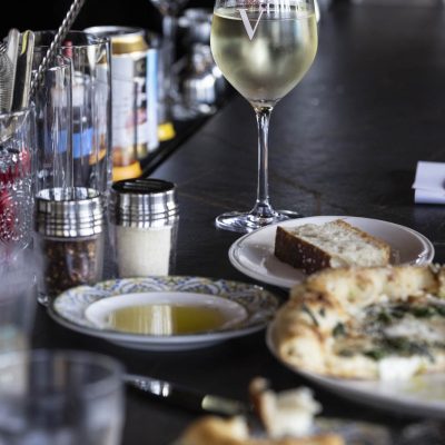 Gathering of appetizers including focaccia with oil and pizza with glass of white wine on bar at Valentina's restaurant in Dublin, Ohio at Bridge Park.