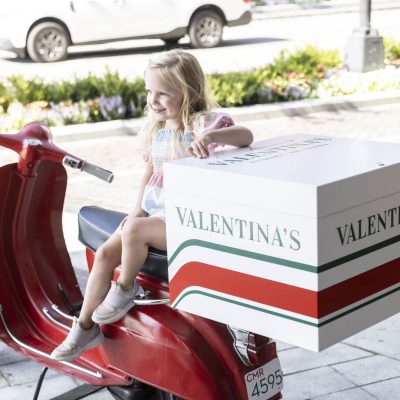 Child sitting on ornamental Vespa scooter outside Valentina's restaurant at Bridge Park in Dublin, Ohio.