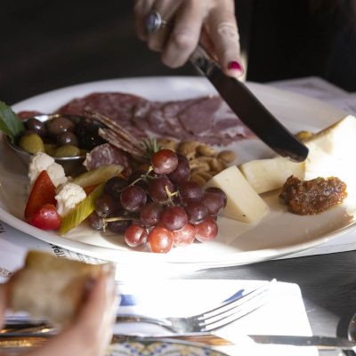 Close up of hand cutting cheese on plate of charcuterie with meats, olives, and fruits at Valentina's restaurant in Dublin, Ohio at Bridge Park.