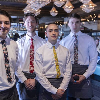 Four servers in colorful ties standing in the dining room at Valentina's restaurant at Bridge Park in Dublin, Ohio.