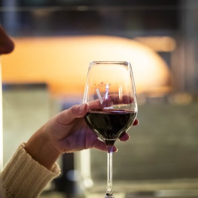 A close of a guest drinking red wine. The glass is embossed with Valentina's 'V' logo.