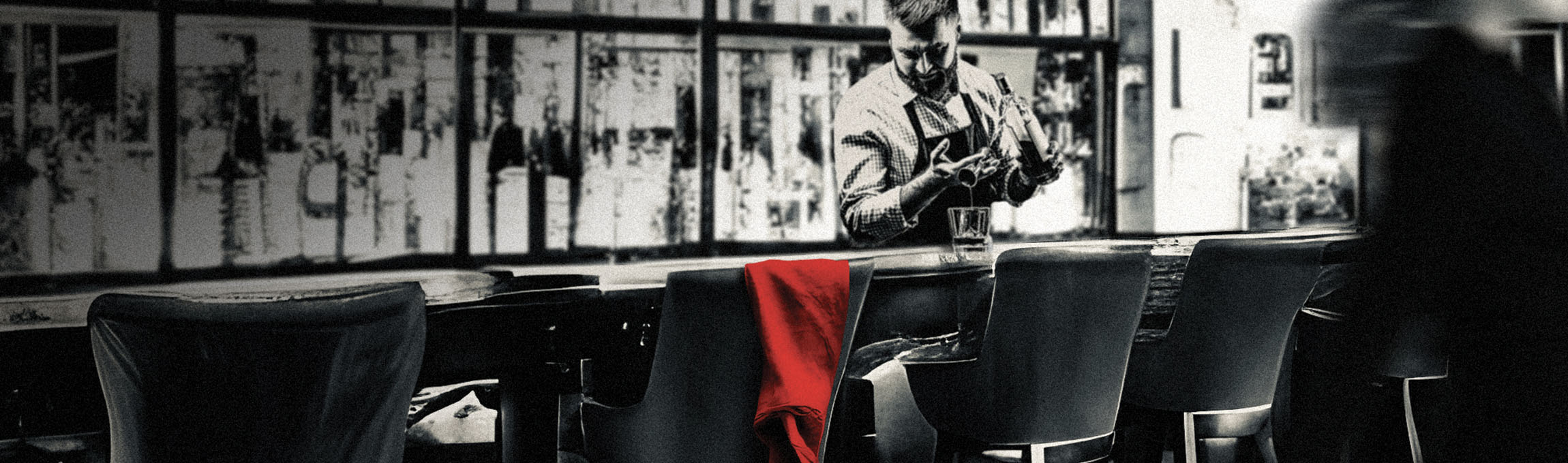 Black and white photo of bartender behind bar, red scarf draped over a barstool as blurred figure of a woman exits right.